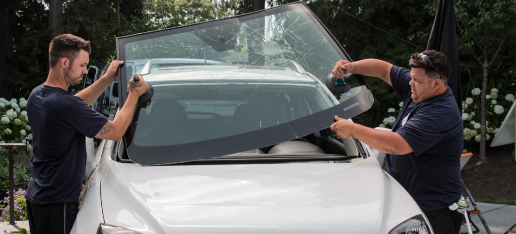 Two technicians remove a broken windshield from a car.